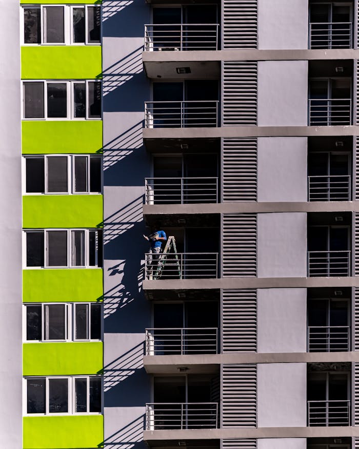 Close-up image of a modern building with balconies featuring a worker on a ladder.