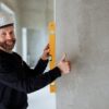 Confident male construction worker using a spirit level on a concrete wall for precise alignment indoors.